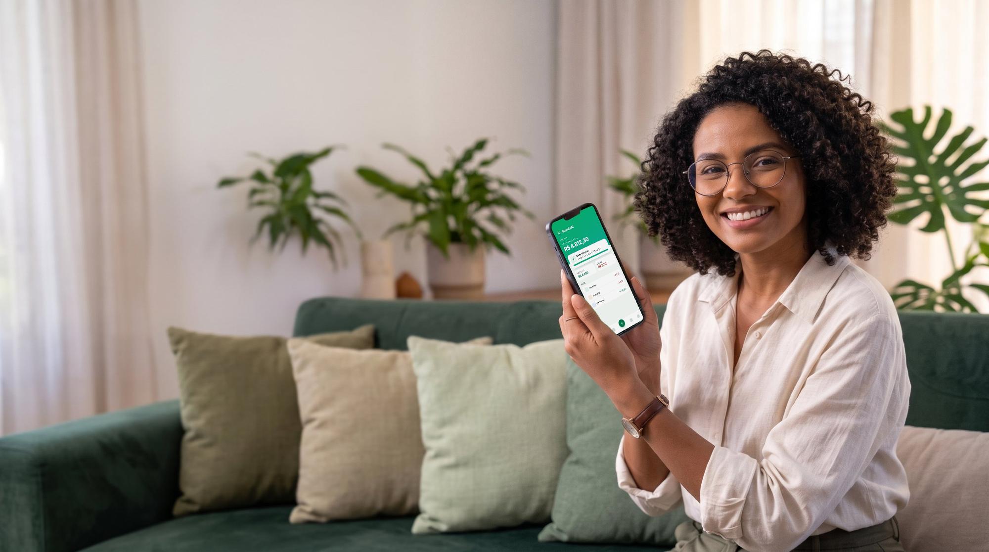 Mulher sorrindo no sofá mostrando a tela do aplicativo GuardaAí no celular